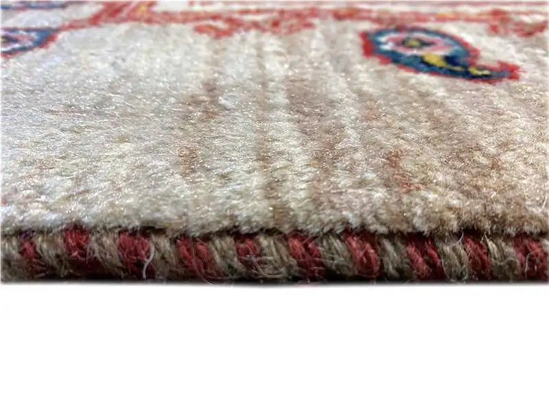 Close-up of the carpet edge: beige pile, red patterned border, and fringe