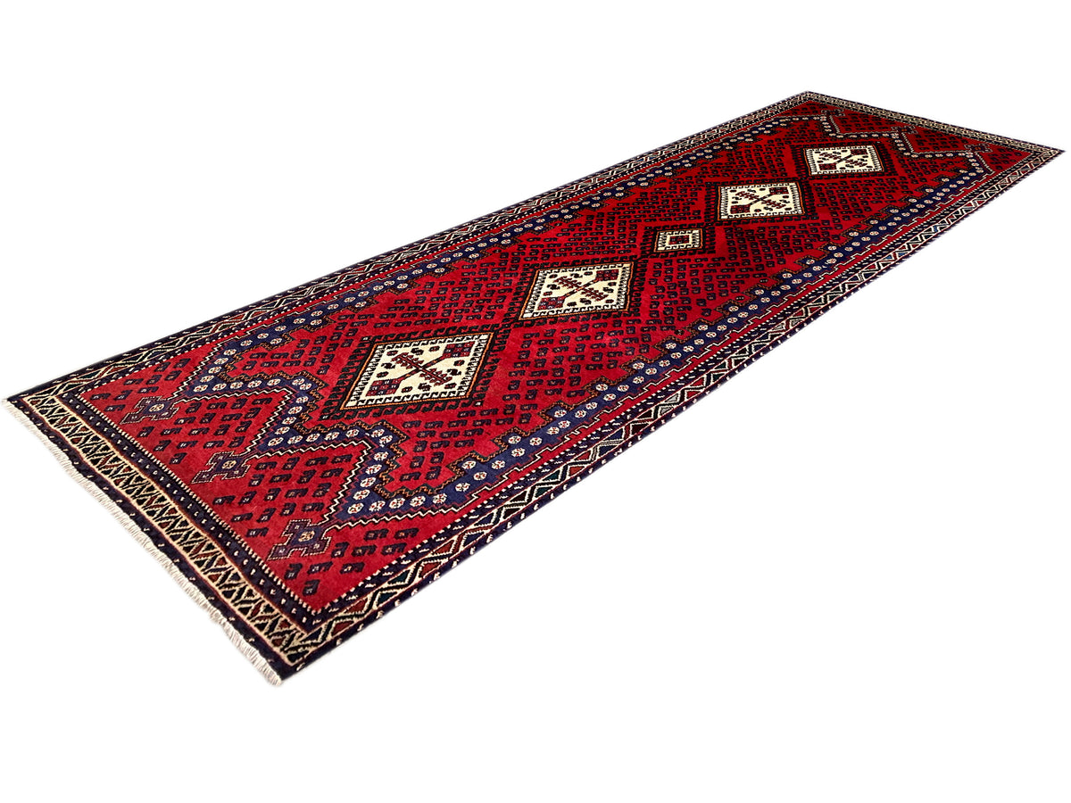 Angled view: red runner rug with geometric panels and a dark blue border