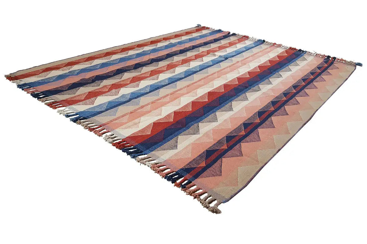Rug shown at an angle with zigzag stripes in blue, red, and beige, with fringes