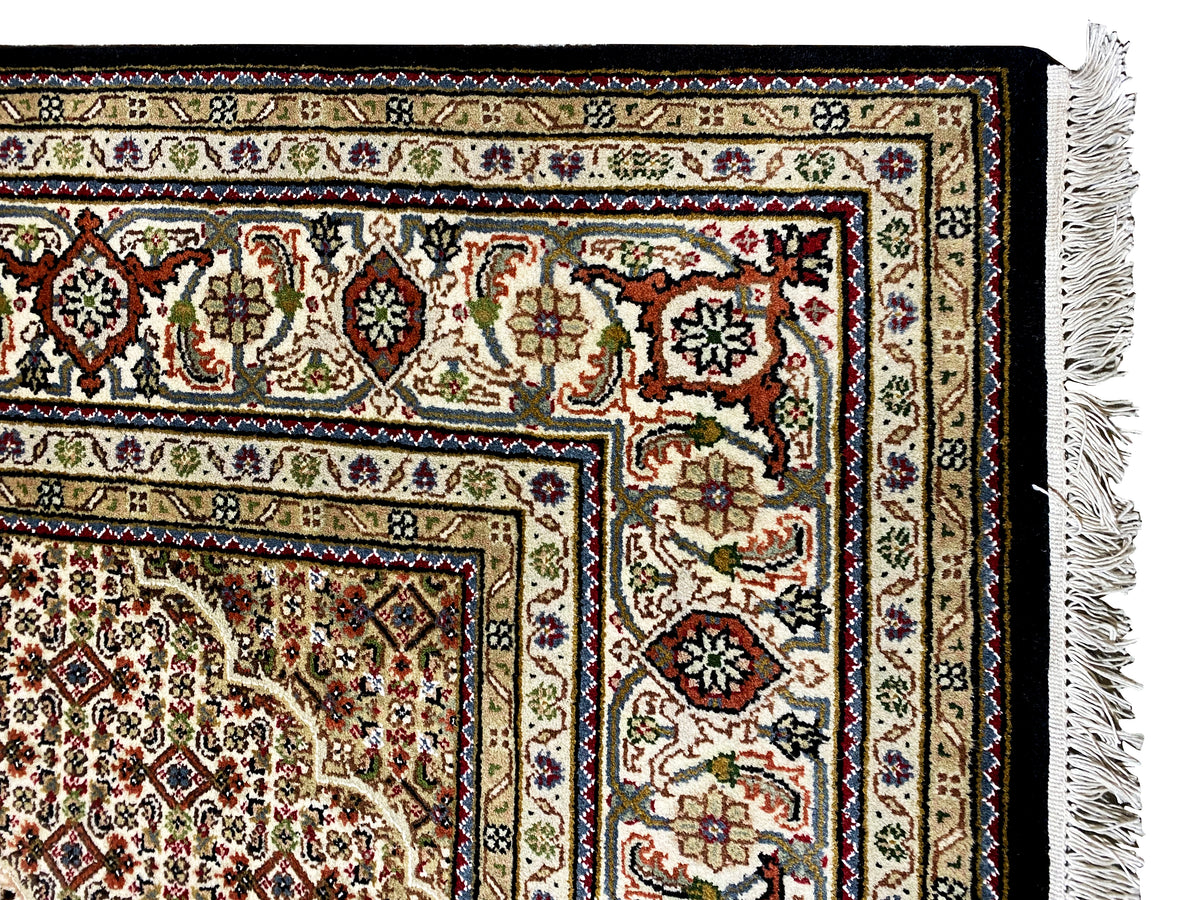 Brown Indo-Tabriz carpet border detail with colorful ornaments and fringe on the right