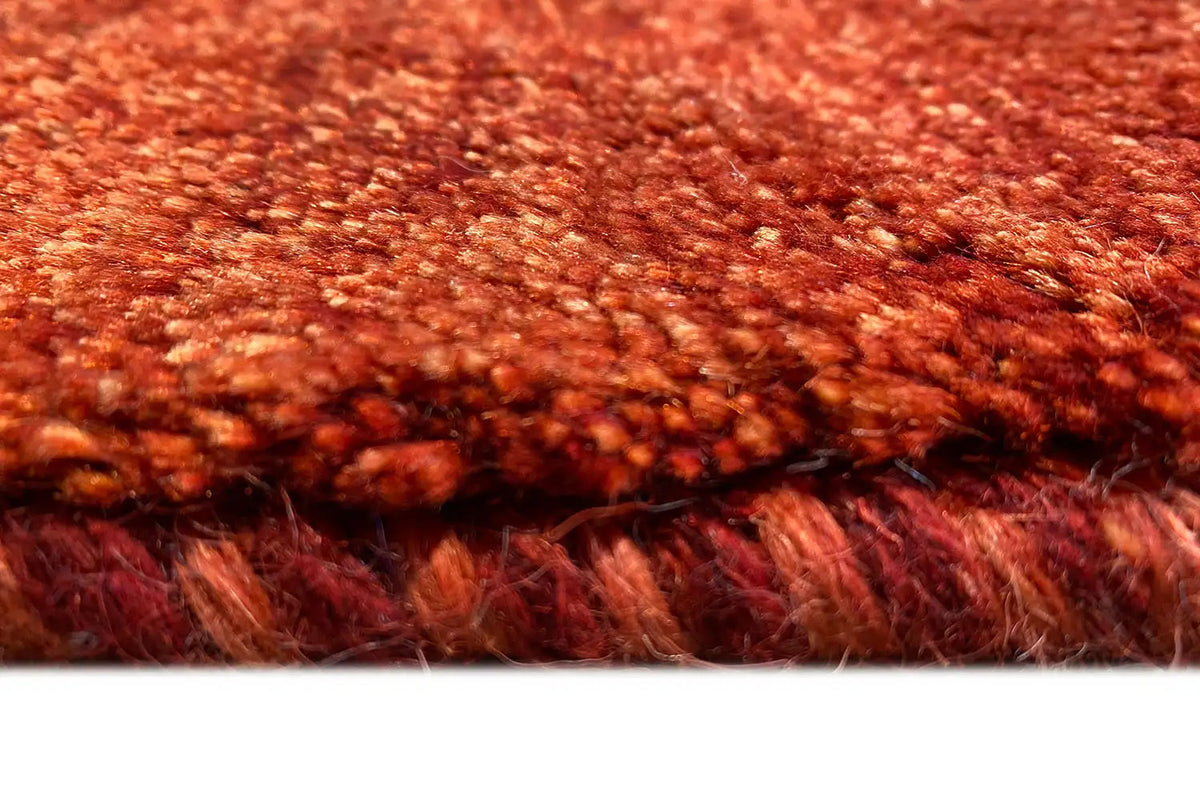 Gabbeh rug close-up: dense red-brown pile, fringes along the edge