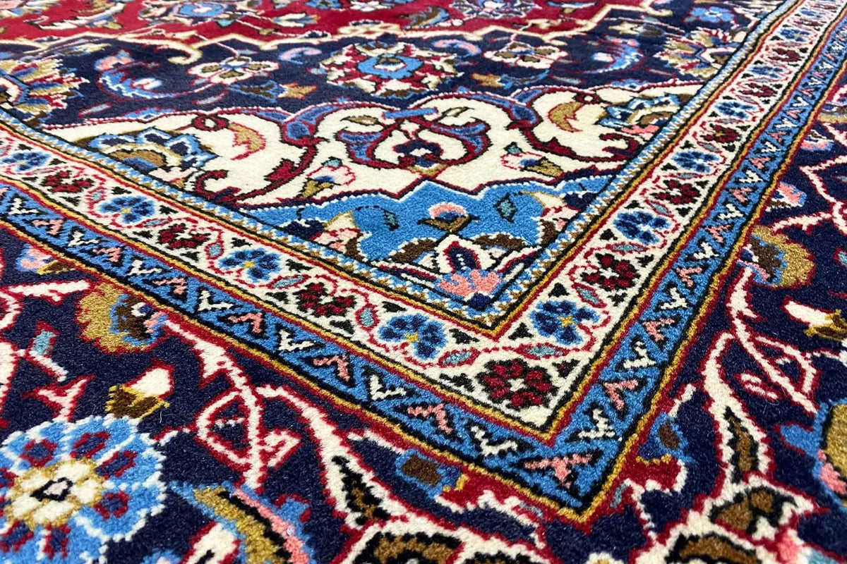 Keshan rug with an ornamental pattern in red, blue, and cream, close-up of the border