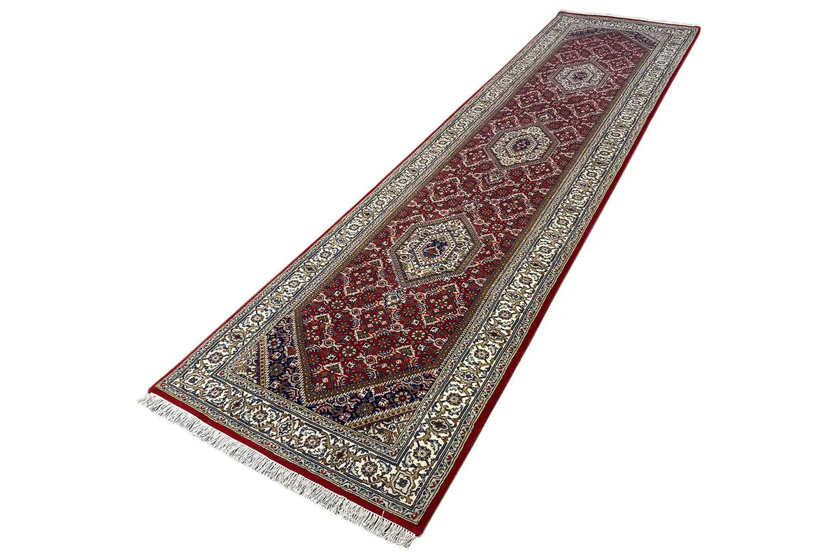Bidjar runner laid out lengthwise with a red background, beige ornaments, and fringes
