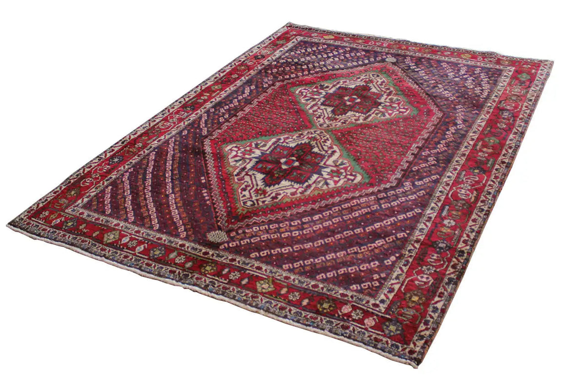 Oriental rug viewed from above at an angle: red central motif, blue pattern, and multicolored edges.