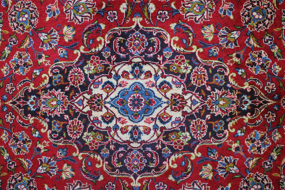 Keshan rug with a red background, a blue-and-white medallion, and colorful garland ornaments