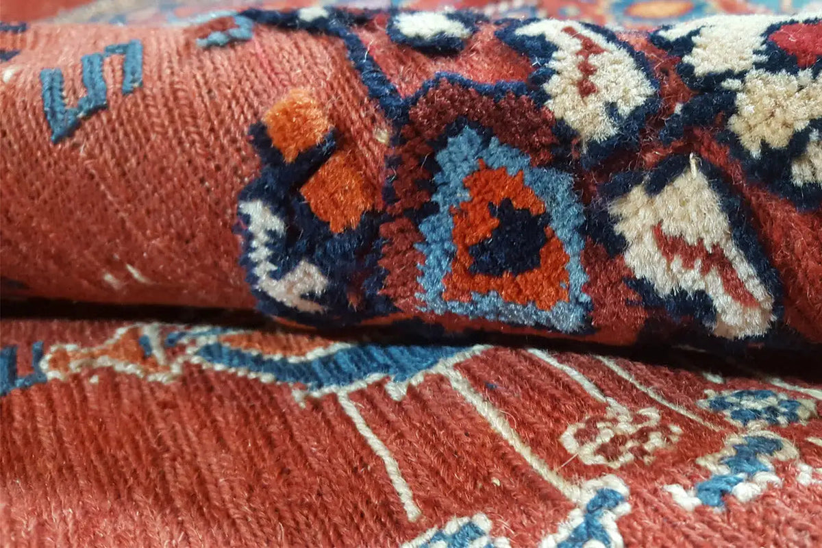 Close-up: reddish carpet pile with blue-orange geometric patterns and fringes