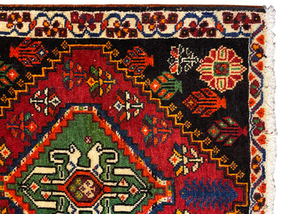 Close-up of a Poshti rug: black rug with a green medallion and colorful ornaments