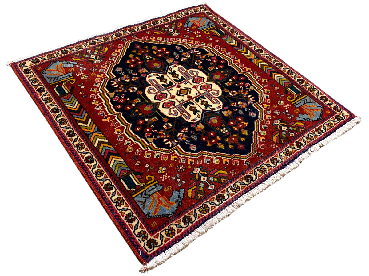 Poshti rug with a red, multicolored pattern and dark center, photographed at an angle