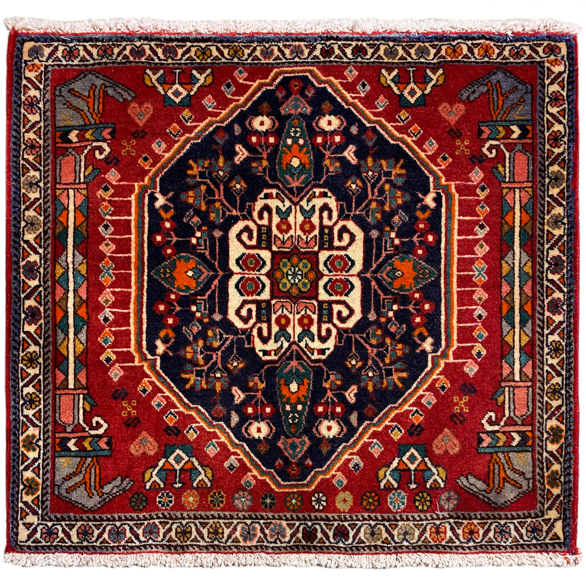 Square rug with a red background and dark blue central motif, with fringes