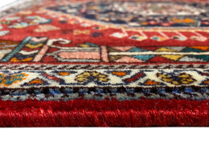 Carpet edge in detail: red pile, multicolored patterned border, and frayed fringe