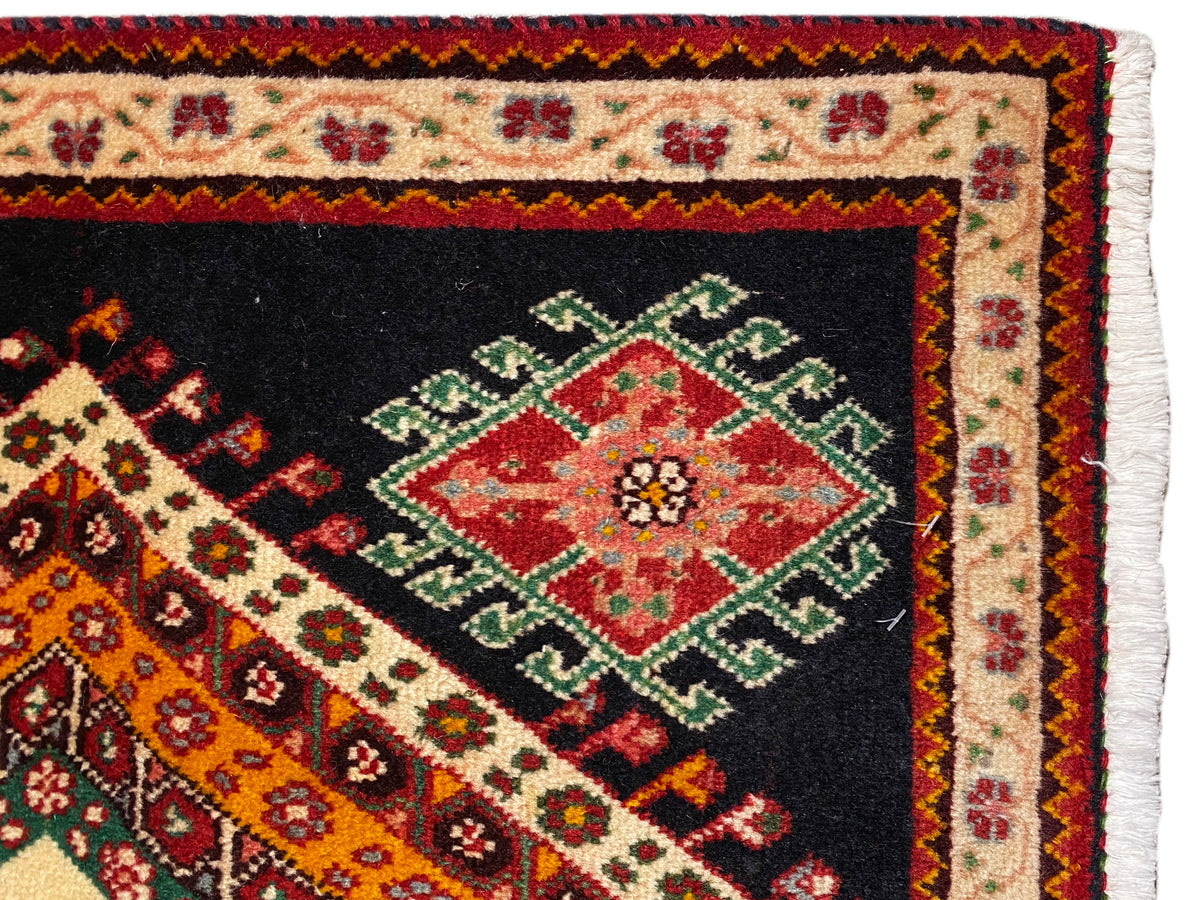 Close-up of Poshti rug: textured edge with fringe and red, green medallion diamond