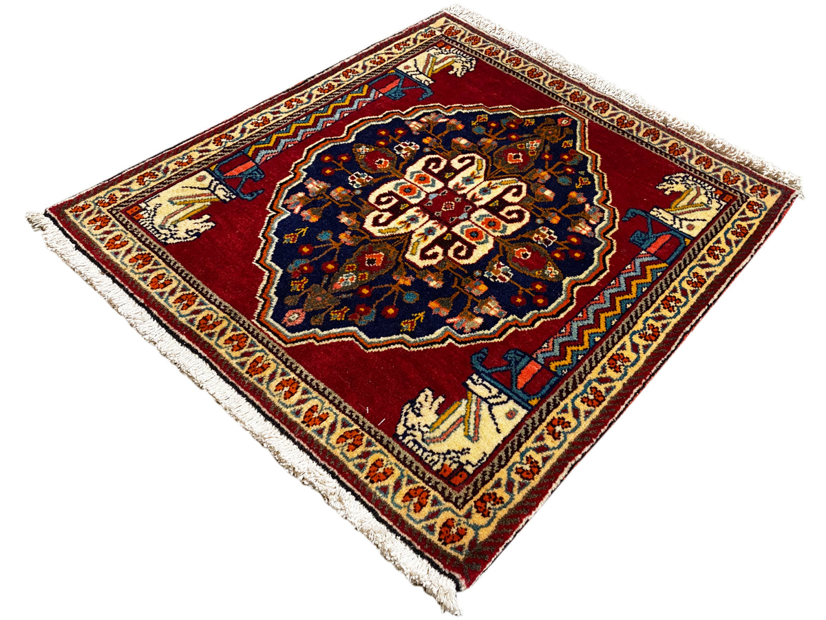 Rug with a red background, dark blue central motif, beige ornamental borders, and fringes