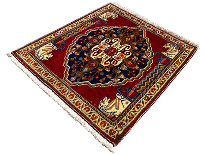 Rug with a red background, dark blue central motif, beige ornamental borders, and fringes