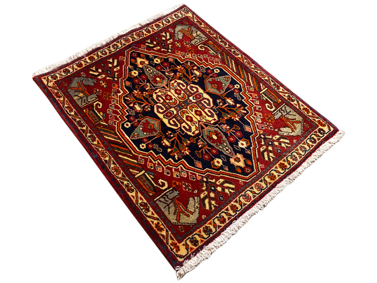 Rug 65x59 cm shown at an angle: red border, dark patterns, fringes on the sides